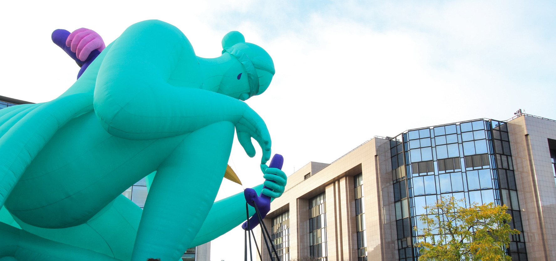 A large, green blow up statue kneeling down, in a city landscape.