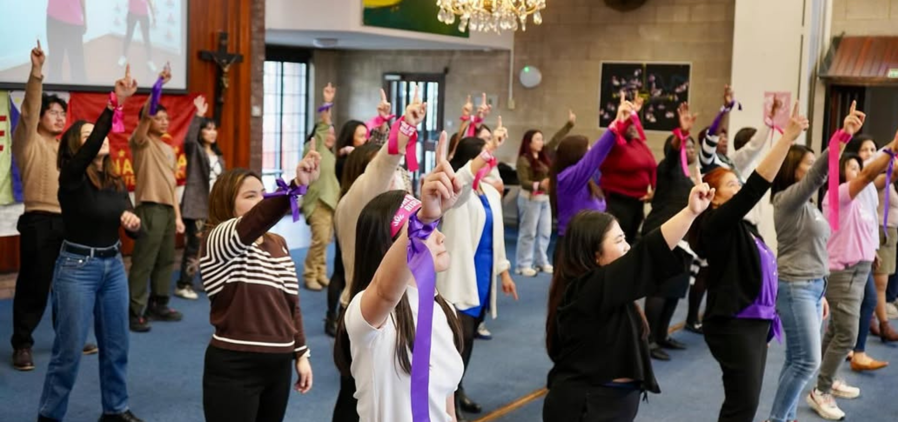 A group of people stood in a room with their arms raised and ribbons tied round their wrists.